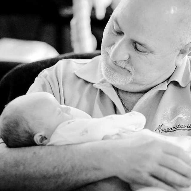 Black and white photo of a grandfather holding his newborn grandson for the first time.