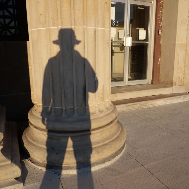 Photo of a person's shadow on the column of an old bank building.