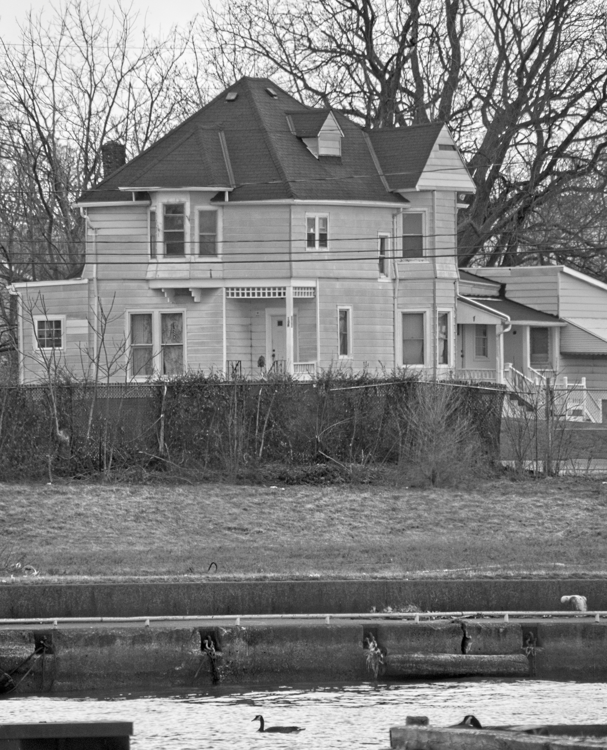 Black and white photo of the oldest house in Lorain overlooking the Black River. Pier and river in the foreground.