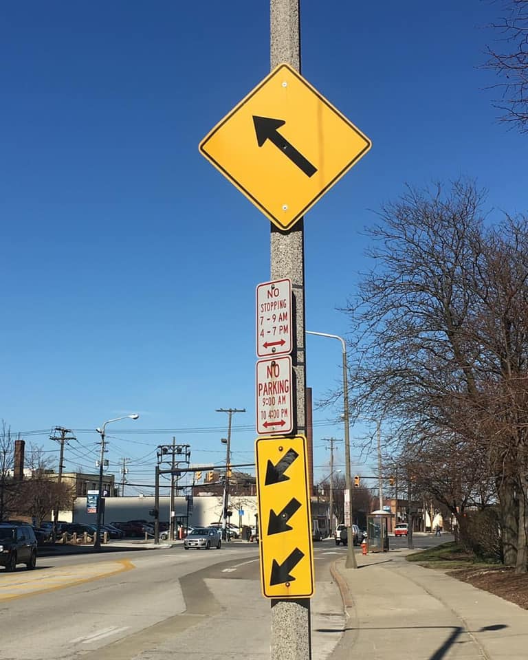 Road signs on a post. One sign is 3 arrows pointing down and another sign is one large arrow pointing up at an angle.